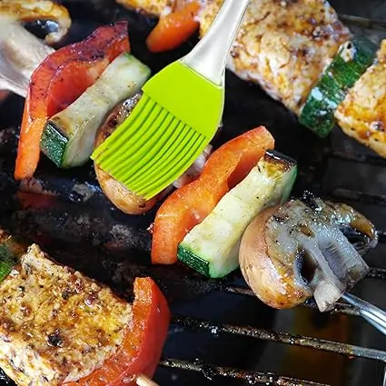 Green silicone basting brush applying marinade to grilled vegetable skewers on a barbecue grill